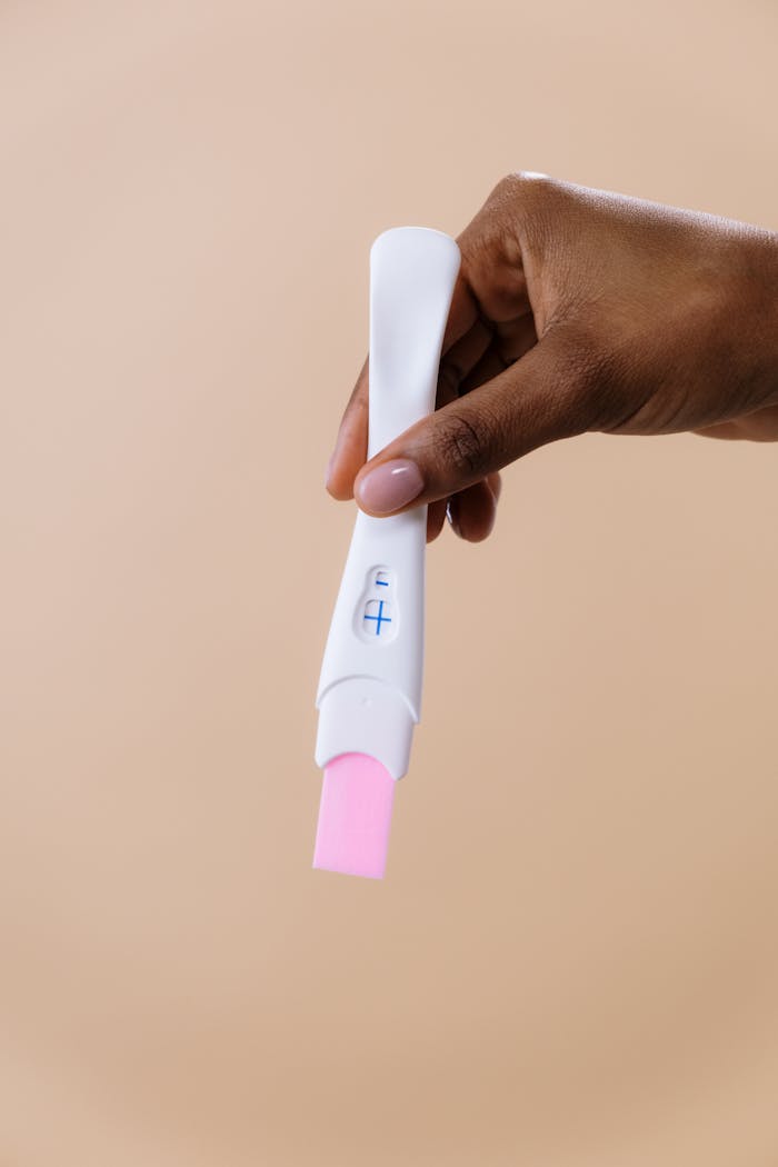our-story A close-up image of a hand holding a positive pregnancy test with a beige background.
